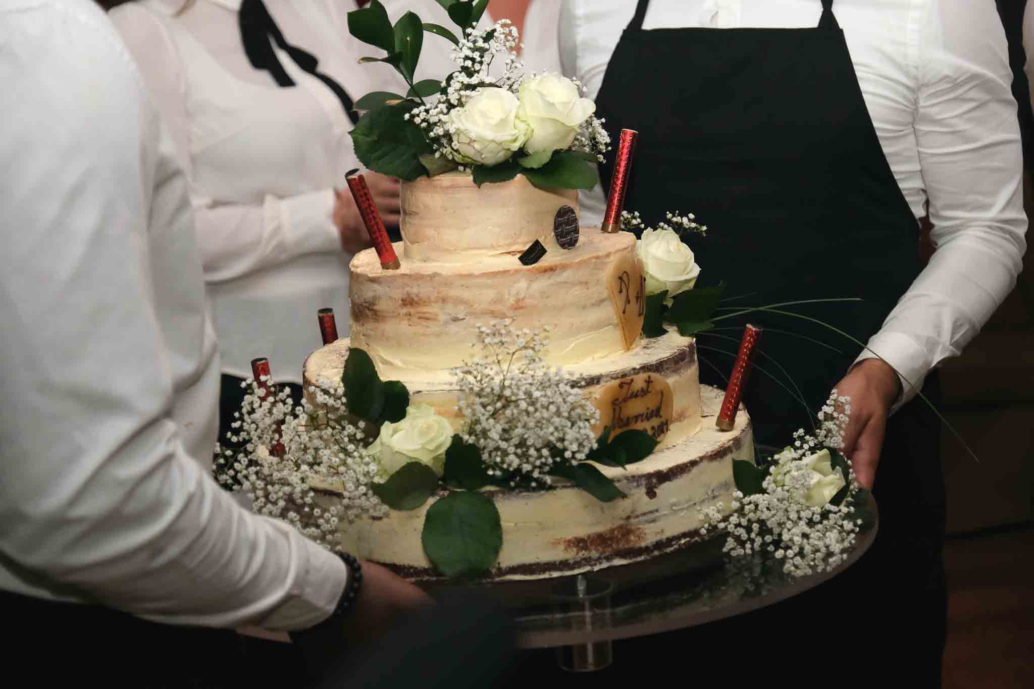 Een mooi gedecoreerde bruilofttaart wordt naar voren gebracht door een paar medewerksters.