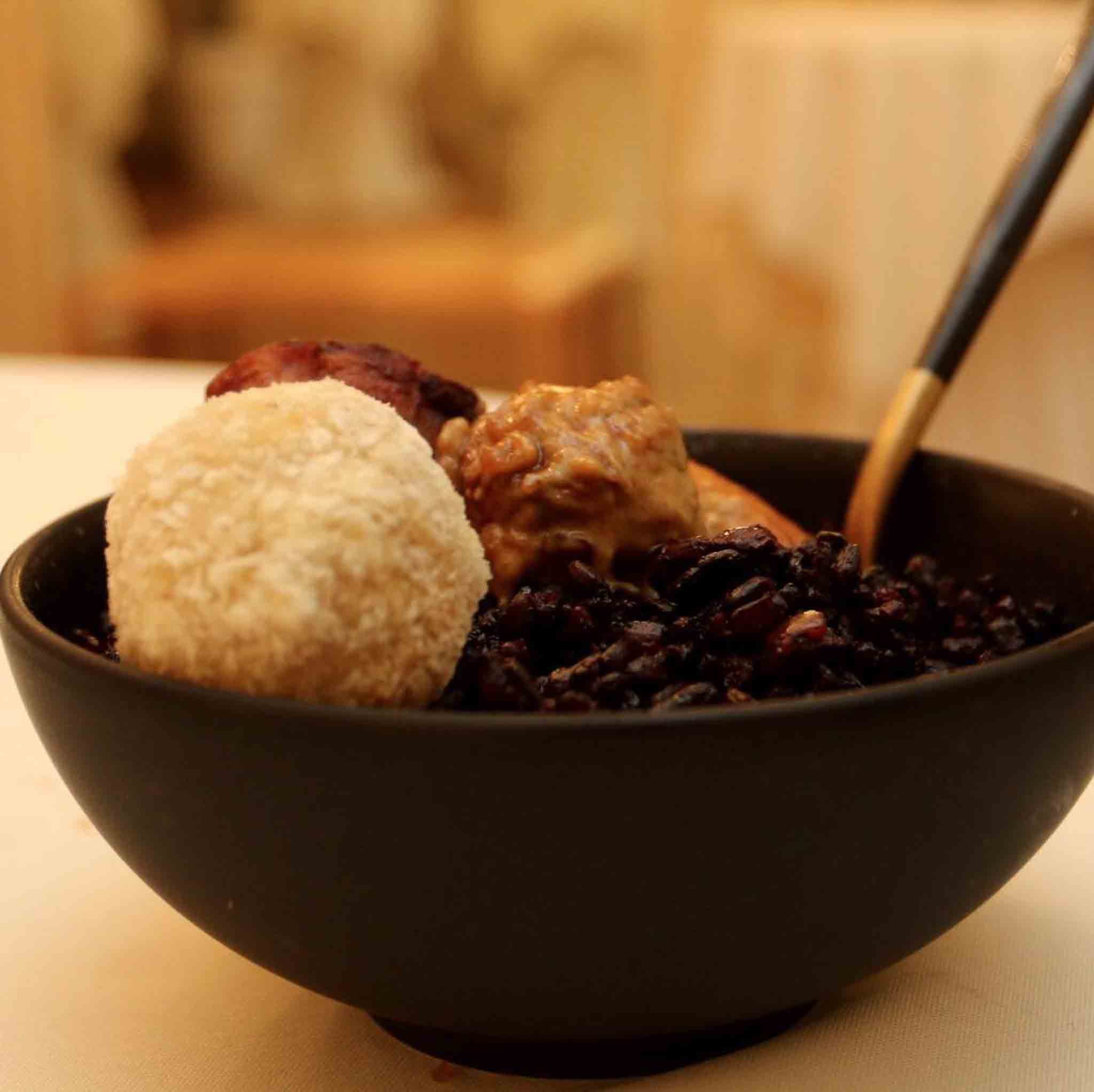 Een houten kommetje van wilde zwarte rijst, kip moambe en zoete aardappel met een kaasballetje.